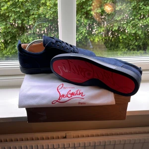 Mörkblå sneakers från Christian Louboutin - Snygga mörkblå sneakers från Christian Louboutin i mocka med klassisk röd sula. Skorna har rund tå, platt sula och snörning. Lyxig känsla med diskret broderad logga på hälen och detaljer i läder på insidan. Perfekta för dig som vill sticka ut med stil. Helt oanvända, perfekt skick👌😁