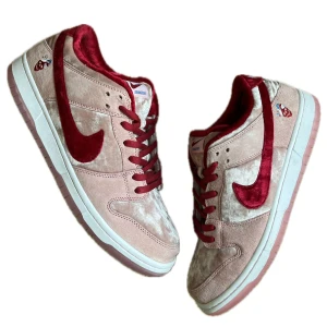 Nike SB Dunk Low StrangeLove - Nike SB Dunk Low 'StrangeLove' med rosa mocka och röd sammet. Swoosh och foder i röd sammet, vit och rosa sula med färgglada detaljer undertill. Unik sneaker i extremt bra skick. Storlek 45. Extra skosnören fås med. Skicket baseras från bilderna. Skriv gärna vid frågor.