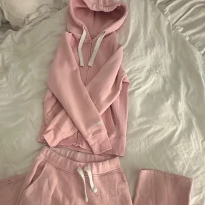 Russemerch mjukissett  - Mysigt mjukissett från Russemerch med huva och vita snören. Tröjan har dragkedja framtill och ribbade muddar vid ärmslut och nederkant. Båda plaggen är i storlek S. Sparsamt använda, men har defekt nere vid byxkanten. Priset kan diskuteras vid snabb och enkel affär!🩷nypris 1250kr.
