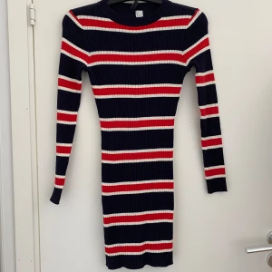 Randig ribbad klänning från H&M, stl 38 - Snygg oanvänd ribbad klänning från H&M Divided i marinblått med röda och vita ränder. Klänningen har lång ärm, rund halsringning och figurnära passform.               Hör av dig vid frågor!                                           Köparen står för frakten. 
