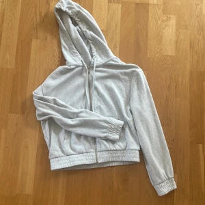 Ljusgrå flecce från H&M Divided - Ljusgrå kort flecce från H&M Divided med dragkedja framtill och huva. Tröjan har långa ärmar, ribbade muddar och två fickor framtill. Perfekt för chill dagar eller när du vill ha en enkel och stilren look. Skriv om ni har några frågor eller vill ha någon bild den är använd ett fårtal gånger så den är i bra skick! Jag säljer den då den inte kommer till användning💞Priset kan diskuteras!