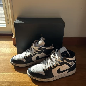 Nike Air Jordan 1 Mid vit/marinblå 42.5 - Säljer ett par Nike Air Jordan 1 Mid i vit och marinblå färg. Klassisk siluett med snörning, rund tå och ikoniska Jordan-loggan på sidan och tungan. Ovandel i skinn och textil, sula i gummi. Perfekta för dig som vill ha en clean och tidlös sneaker. Original Box och extra snören medföljer. Priset går såklart att diskuteras.