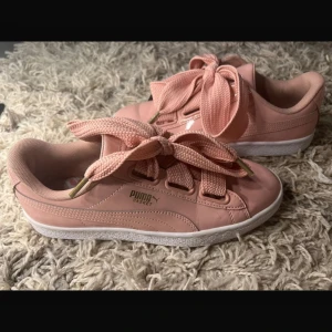 Puma sneakers  - Snygga rosa Puma Basket sneakers i glansigt lackmaterial med breda matchande skosnören och vit sula. Guldiga detaljer vid snörningen och klassisk låg modell. Silkes snören medföljer. Perfekta för dig som vill sticka ut med en feminin touch och sportig vibe.