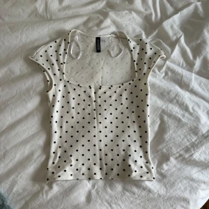 Prickig topp från H&M Divided - Supersöt vit topp med svarta prickar från H&M Divided. Modellen är croppad med korta ärmar och fyrkantig urringning. Storlek xxs men passar xs och s. Perfekt att styla med jeans eller kjol till en sommarkväll! 