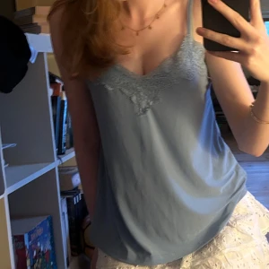 Ljusblå linnetopp med spets från New Yorker - Supersöt ljusblå linnetopp från New Yorker med tunna axelband och v-ringning dekorerad med spets. Perfekt för varma dagar eller lager på lager. Sval och mjuk känsla, lätt att matcha med både jeans och kjol.