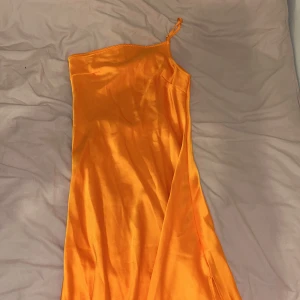 Orange långklänning Forever 21 - Snygg orange långklänning från Forever 21 köpt i Dubai i glansigt satintyg. Klänningen har en asymmetrisk axel med ett smalt axelband och en slits på sidan. Perfekt för dig som vill sticka ut med en färgstark och trendig look. Perfekt för dig som är tanned😜