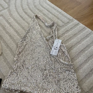 Glittrig silver paljettopp Gina Tricot - Supersnygg glittrig topp från Gina Tricot i silver med massor av paljetter. Toppen är ärmlös och har smala axelband som korsas i ryggen. Perfekt för dig som vill sticka ut och glänsa på nästa fest!