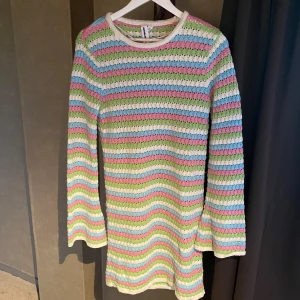 Pastellrandig stickad kortklänning - Superfin stickad kortklänning med pastellfärgade ränder i vitt, rosa, blått och grönt. Klänningen har lång ärm och en rund halsringning. Perfekt för dig som gillar färg och retrovibbar!