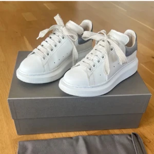  Alexander McQueen sneakers - Snygga vita sneakers från Alexander McQueen med chunky plattformssula och ljusgrå mockadetalj på hälen. De är i väldigt fint skick, snörena är lite slitna men de går att fixa nya! Box och dustnag kommer med!