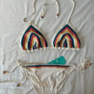 Färgglad virkad bikini från H&M - Superfin bikini från H&M med virkade detaljer i vitt, blått, rosa och gult. Toppen har trekantsform och knytband med färgglada pärlor. Underdelen har matchande virkade ränder och knyt i sidorna. Perfekt för stranden och sommarens alla bad