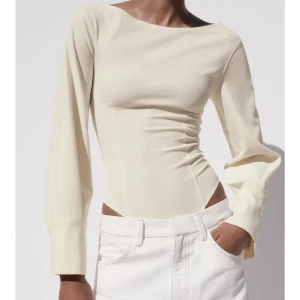 Beige korsettbody med öppen rygg  - Säljer en stilren beige långärmad topp med tight passform och snygg öppen rygg. Toppen har en asymmetrisk halsringning och är tillverkad i ett mjukt, stretchigt material som sitter riktigt snyggt på kroppen. Perfekt för dig som gillar minimalistisk och trendig stil.
