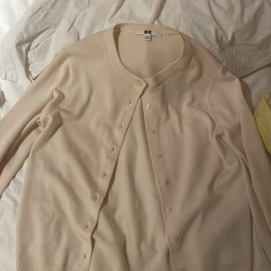 Beige kofta från Uniqlo XS - Snygg beige kofta från Uniqlo i storlek XS. Klassisk rund halsringning, långa ärmar och knappar framtill. Mjuk och tunn, perfekt att slänga över en t-shirt eller linne.