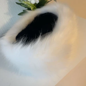 Vit pälsmössa i klassisk stil - Supermjuk och fluffig vit pälsmössa med rund form och bred kant. Perfekt för dig som vill sticka ut med en elegant vinterlook. Mössan har en lyxig känsla och är helvit med lång luggig päls. Passar perfekt till kalla dagar.