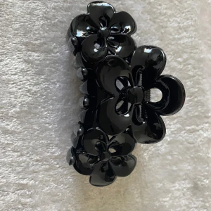 Svart hårklämma med blommor - En svart hårklämma i glansig plast med stora blommor som dekoration. Klämman har en cool och stilren look med blommor på ovansidan och stark fjäder för bra grepp. Perfekt accessoar för att lyfta din frisyr. 35kr/st . Ny . Finns fler kvar 