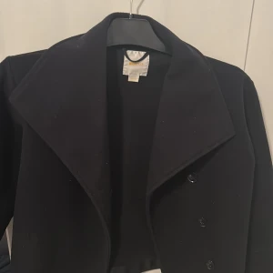 Svart kappa från Gina Tricot - Stilren svart kappa från Gina Tricot med bred krage och knäppning framtill. Klassisk design som passar perfekt till lager-på-lager. Perfekt för lite kyligare dagar. Säljer då den är för liten för mig. Köpt för ungefär två år sedan💕