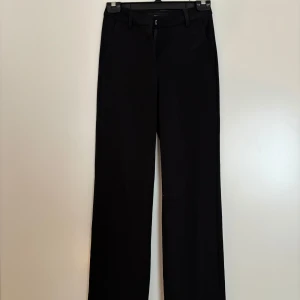 Svarta kostymbyxor från Veromoda - Klassiska svarta kostymbyxor från Veromoda i rak modell. Byxorna har bälteshällor, snedställda fickor och stängs med dragkedja och hake. Perfekta för en clean och stilren look. Materialet är mjukt och följsamt för extra komfort.