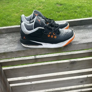 Svarta Nike Air Jordans med orange detaljer - Snygga svarta Nike Air Jordans med orange detaljer och vit sula. Skorna har lågt skaft, perforerad tå och grå insida. Klassisk Jumpman-logga i orange på plösen och sidan. Perfekta för dig som vill sticka ut med en sportig och cool look.