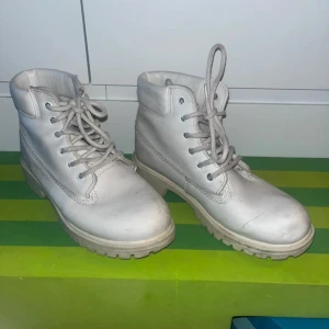 Vita boots med snörning, storlek 36 - Coola vita boots med grov sula och snörning hela vägen upp. Skorna har rund tå och är tillverkade i syntetmaterial med vadderad kant upptill för extra komfort. Perfekta för dig som vill ha en clean och stilren look till höst och vinter.