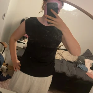 Svart ärmlös topp från H&M - Svart ärmlös topp från H&M i storlek L. Toppen har en enkel och stilren design med rund halsringning och lätt rynkade detaljer på ena sidan för en snygg twist. Tillverkad i ett mjukt och stretchigt material som känns skönt mot huden.