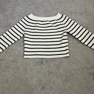 Randig stickad tröja i vitt och svart - Snygg stickad tröja med svarta ränder på vit botten. Tröjan har lång ärm, bred halsringning och är croppad i modellen. Perfekt för dig som gillar en klassisk men trendig look. Materialet är mjukt och stretchigt stickat tyg. Minns inte vart jag köpte den- men den är super fin