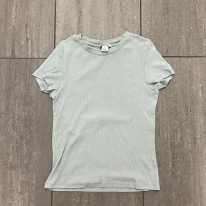 Ljusblå ribbad topp från Monki - En basic ljusblå ribbad topp från Monki i mjuk bomull. Modellen har rund halsringning och korta ärmar, perfekt för en clean och enkel look. Snygg att styla med jeans eller kjol för en chill vibe.