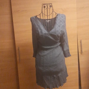 Mörkblå omlottklänning KappAhl L - Supersnygg mörkblå kortklänning från KappAhl med v-ringning, broderade detaljer upptill och knytband i ryggen. Klänningen har trekvartsärm och volangkant nertill. Perfekt för dig som gillar en feminin och bekväm stil.