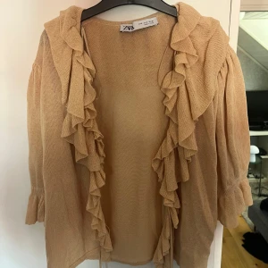Beige volangkofta från Zara, stl S - Superfin beige kofta från Zara med volangdetaljer längs hela kanten. Koftan är stickad och har en loose passform med trekvarts ärmar 💕
