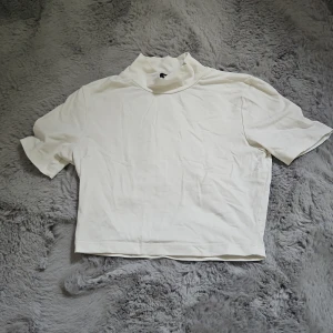 Polotopp - En stilren vit polotopp med korta ärmar och croppad passform. Toppen har en hög krage. Storlek XS men passar XXS också. Knappt använd. Skriv om du har funderingar.