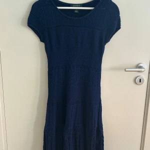 Mörkblå stickad klänning Lauren Ralph Lauren - Mörkblå stickad klänning från Lauren Ralph Lauren med kort ärm och rund hals. Klänningen har ett snyggt strukturerat mönster och är i mjukt stickat material. Perfekt för dig som gillar klassisk och stilren look.