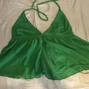 Grön halterneck linnetopp - Snygg grön linnetopp med halterneck och v-ringning. Toppen har broderade detaljer i tyget och knappar framtill. Luftig och lätt, perfekt för varma dagar. Den har en lös passform och är ärmlös med tunna knytband i nacken.