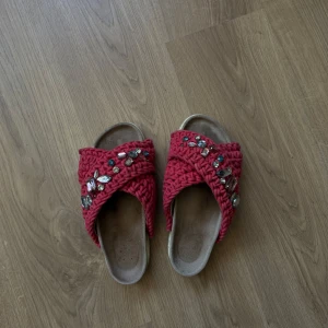 Röda sandaler från Inuikii med pärlor - Unika sandaler från Inuikii i röd stickat material med breda korslagda band och stora glittrande pärlor och stenar. Platt sula och öppen tå, perfekt för att sticka ut i sommar. Superbekväma och snygga till jeans eller klänning.