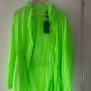 Neongrön vindjacka från Brave Soul - Säljer en riktigt fet neongrön vindjacka från Brave Soul. Jackan har dragkedja, snörning i midjan och huva. Perfekt för dig som vill sticka ut och hålla dig skyddad mot vinden. Lätt material och avslappnad passform.