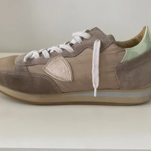 Philippe Model beige sneakers mocka - Snygga sneakers från Philippe Model i beige och ljusgrönt med detaljer i mocka, textil och skinn. Skorna har vit snörning, gummisula och klassisk rund tå. Ända defekten är lite slitage i sulan men det märks knappt.