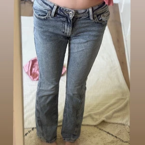Blå bootcut jeans med broderade fickor - Snygga blå bootcut jeans med coola broderade detaljer på bakfickorna. Jeansen har låg midja och klassisk femficksmodell. Perfekta för dig som gillar en avslappnad men ändå trendig look.