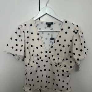 Prickig blus med puffärm från Boohoo - Supersöt blus från Boohoo, créme vit med svarta prickar. Modellen har v-ringning och korta puffärmar. Ny med prislapp.