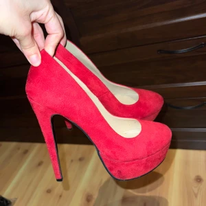Röda mocka pumps med platå och hög klack - Snygga röda pumps i mocka med riktigt hög klack och platåsula. Skorna har rund tå och en klassisk siluett som verkligen sticker ut. Perfekta för dig som vill ha statement heels med extra höjd och stil.
