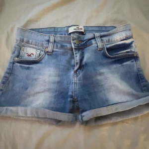 Hollister jeans shorts - Snygga blå jeansshorts från Hollister med uppvikta benslut och klassisk femficksdesign. Shortsen har en ljus tvätt och logga på myntfickan. Perfekta för varma dagar och enkel att matcha med allt. 