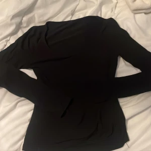 Svart långärmad topp - En stilren svart långärmad topp med enkel design. Tight passform som sitter snyggt på kroppen och passar perfekt till jeans eller kjol. Mjuk och stretchig känsla, vilket gör den bekväm att bära hela dagen.