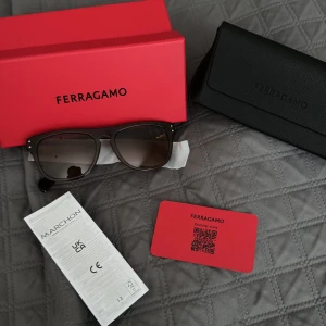 Bruna solglasögon från Ferragamo - Snygga solglasögon från Ferragamo i brun transparent acetat med fyrkantig form. Sidorna har en diskret silverdetalj och logga. Kommer med originaletui och ask. Perfekta för dig som vill ha en stilren och lyxig look. Passade ej mig därför jag säljer här endast testat, nytt pris 3015kr