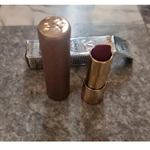 Lancôme L'Absolu Rouge Läppstift 155 - Snyggt läppstift från Lancôme i nyansen 155 Burning Lips. Färgen är en djup vinröd med matt finish. Hylsan är lyxig i guld och brons med rosdetalj på locket. Oanvänt,  men kartongen har blivit "knölig".
