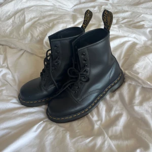 Svarta Dr. Martens 1460 boots - Klassiska svarta Dr. Martens 1460 boots i skinn med gul söm runt sulan och högt skaft. Ikoniska dragflikar med logga baktill och snörning framtill. Perfekta för dig som vill ha en edgy och tidlös stil. Oanvända! Nypris ca 1400kr