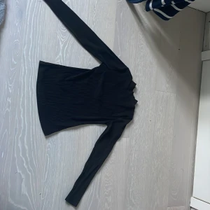 Svart ribbad polotröja med struktur. - Säljer en svart ribbad polotröja med lång ärm och hög krage. Tröjan har en snygg strukturerad yta och är figurnära i modellen. Perfekt att styla med jeans eller kjol för en clean look.