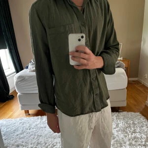 Mörkgrön skjorta i linne från H&M - Säljer en olivgrön skjorta från "These Glory Days", passar perfekt nu till sommaren. 