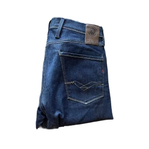 Replay Anbass jeans  - Säljer ett par snygga Replay Anbass jeans i mörkblå tvätt. Modellen har klassisk femficksdesign, raka ben och diskreta kontrastsömmar. Jeansen är tillverkade i bomull med en skön stretch och passar perfekt till en avslappnad stil. Längd ca 111cm mycket bra skick förutom tråden som syns på bakfickan på bild 1
