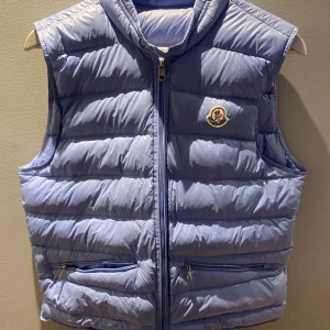 Ljusblå dunväst från Moncler - Säljer min fina väst ifrån moncler! Den är i unisex men jag skulle säga att den är lika snygg på tjejer som killar. Perfekt att ha på sig nu i sommar eller till höst!💞 skriv för fler bilder eller om ni undrar något💗 västen är i storlek 1 som motsvarar S 