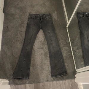 Gråa jeans Bershka - Säljer ett par gråa jeans från Bershka med en boot cut och fin passform. De har en låg midja, klassiska femficksdesign och tydliga kontrastsömmar i vitt. Byxorna är tillverkade av bomull och elastan för extra komfort och stretch. Passar perfekt för en casual look och har en snygg, något slitstark finish.