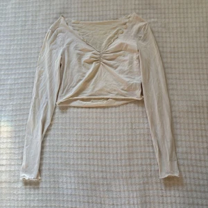 Vit croppad långärmad topp - Den har 2 fläckar som kanske går bort i tvätten har ej testat! Säljer den här vita croppad topp med lång ärm och v-ringning. Toppen har rynkdetalj framtill och vågig kant vid halsen. Tillverkad i mjukt bomullsmaterial, perfekt för en chill och stilren look.