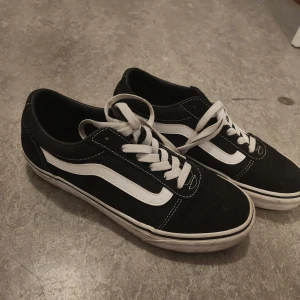Svarta och vita Vans sneakers - Knappt använda, tvättad. Klassiska Vans sneakers i svart med vita detaljer och snörning. Skorna har den ikoniska vita sidoremsan och platt sula. Perfekta för en avslappnad streetstil och passar till det mesta i garderoben.