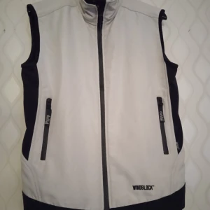 Vit och svart windblock-väst deVal XS - Snygg vit och svart väst från deVal i storlek XS. Västen har hög krage, hel dragkedja framtill och två fickor med dragkedja. Windblock-tyg som skyddar mot vind, perfekt för utomhusaktiviteter. Sportig look med svarta detaljer längs sidorna och fickorna. Västen är ny skick oanvänd. 369: kr. Kan skickas med extra pris via post.