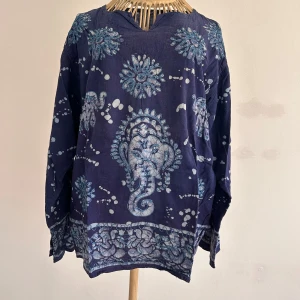 Mörkblå bomullstunika med elefantmönster - Säljer en unik mörkblå tunika i 100% bomull med vackra elefantmönster i ljusare nyans. Tunikan har långa ärmar och en avslappnad passform, perfekt för en bohemisk stil. Tillverkad i Indien. Passar M och även S/M.